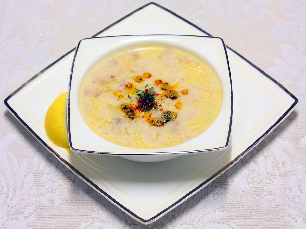 Marinierte Fleischsuppe mit Gewürzbutter in einer weissen Schale, daneben Zitrone