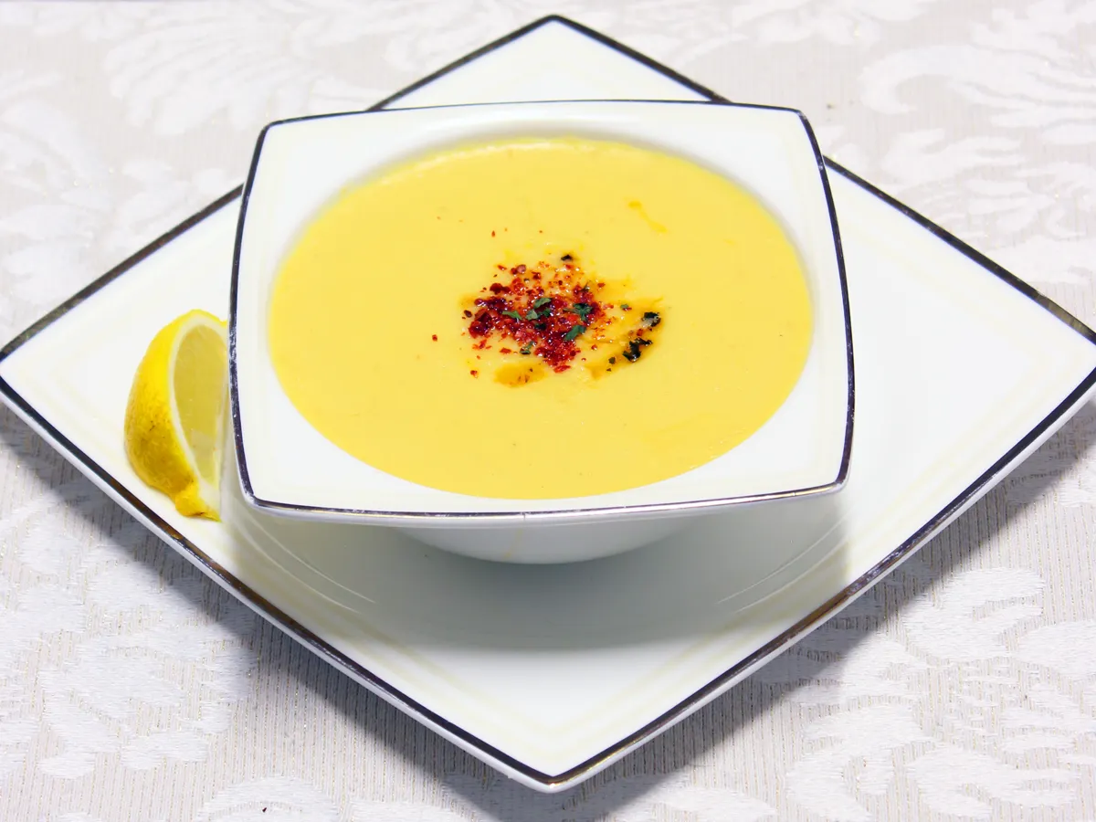 Linsensuppe mit Paprikapulver in einer weissen Schale, daneben eine Zitronenscheibe