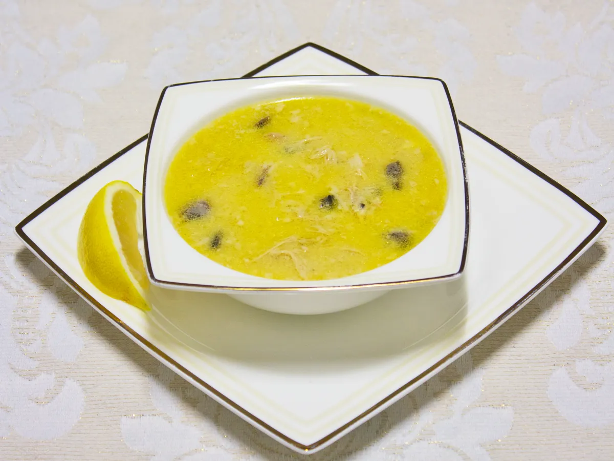 Cremige Pouletsuppe mit Pilzen in einer weissen Schale, daneben Zitrone